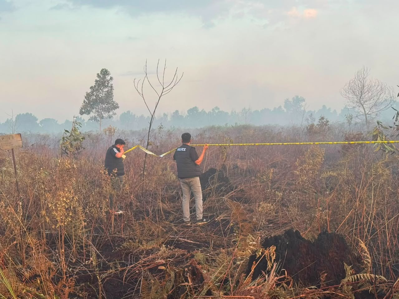 Petugas Satreskrim Polres Kubu Raya memasang garis polisi (police line) di lahan gambut seluas sekitar 4 hektare yang terbakar di depan SMAN 4 Sungai Raya, Desa Limbung, Rabu (15/7/2026). Penyegelan dilakukan untuk menjaga status quo lokasi guna kepentingan penyelidikan dugaan tindak pidana karhutla. Foto: Istimewa