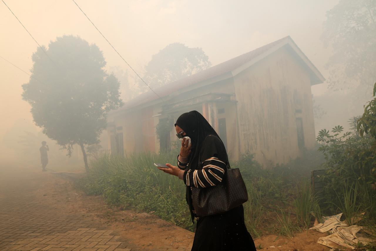 Seorang warga menutup hidung saat melintas di tengah asap akibat kebakaran hutan dan lahan (karhutla) yang mendekati permukiman di Kecamatan Sungai Raya, Kabupaten Kubu Raya, Kalimantan Barat, Rabu (5/8/2026). Foto: Antara